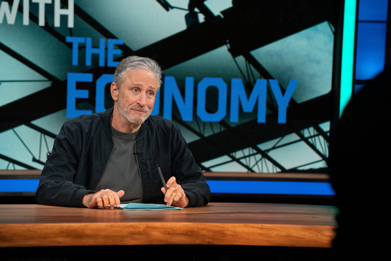 jon stewart seated behind a desk