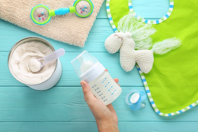 Woman holding feeding bottle of baby milk formula on wooden background