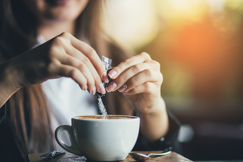 A woman pouring sugar in a coffee cup.