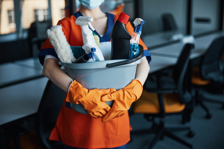 A person holding a plastic bucket with cleaning supplies.