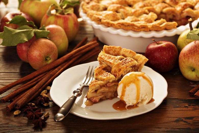 Piece of an apple pie with ice cream scoop and caramel sauce on a plate, fall baking concept.