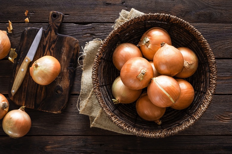 Fresh onions in basket on wooden table, top view