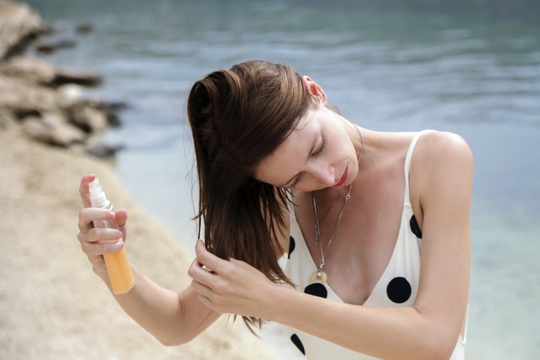 Woman applying sunscreen spray on her hair at the beach.