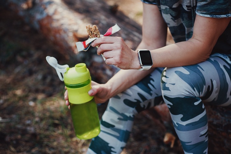 A woman eating a protein bar and hydrating during exercise.
