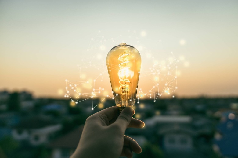 hand holding lightbulb with sun setting in background, electricity concept