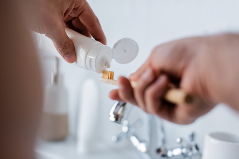 A person squeezing toothpaste on toothbrush in the bathroom.